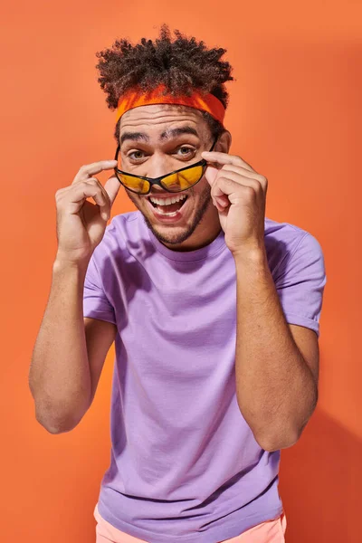 Homem americano africano alegre na cabeça sorrindo e vestindo óculos de sol no fundo laranja — Fotografia de Stock