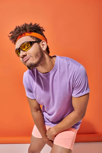 Funny african american man in eyeglasses and headband pouting lips on orange background — Stock Photo