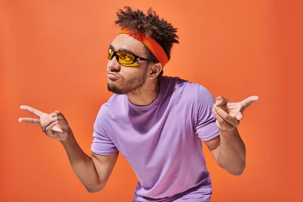 African american man in eyeglasses and headband pouting lips and gesturing on orange background — Stock Photo