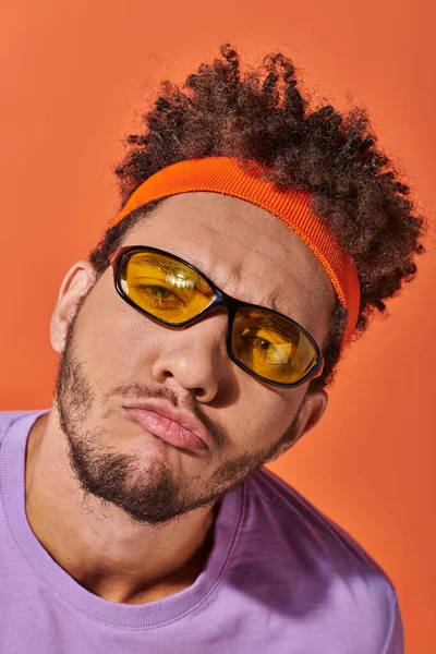 Lustiger afrikanisch-amerikanischer Mann mit Brille und Stirnband schmollende Lippen auf orangefarbenem Hintergrund, Fratze — Stockfoto