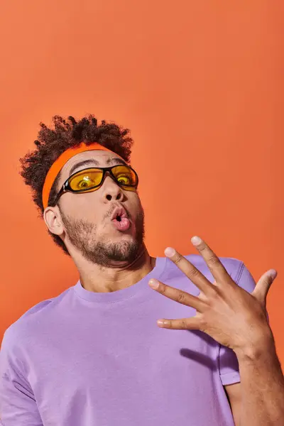 Surprised african american man in eyeglasses and headband looking at camera on orange background — Stock Photo