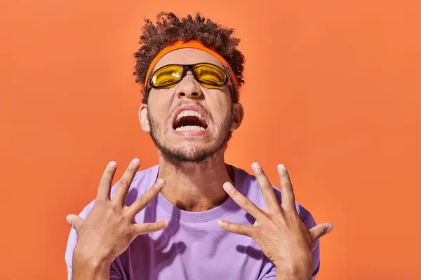 Emotionaler afrikanisch-amerikanischer Mann mit Stirnband und Sonnenbrille gestikuliert auf orangefarbenem Hintergrund — Stockfoto