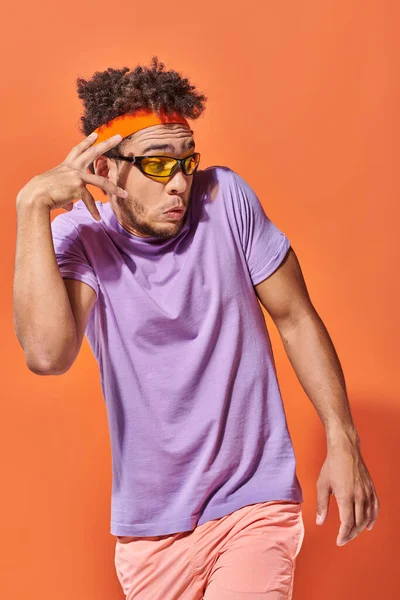 Surprised african american man in eyeglasses and headband looking away on orange background, gesture — Stock Photo