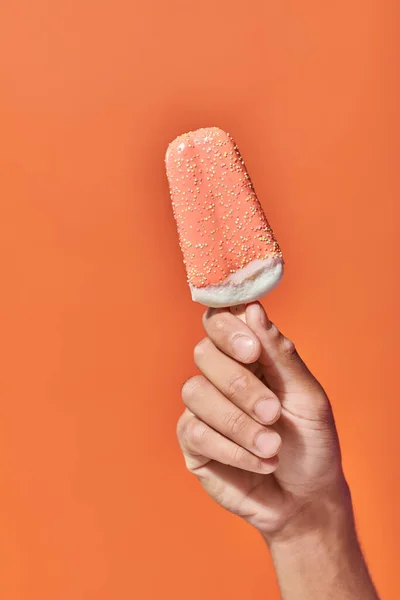Tiro recortado de la persona que sostiene helado helado helado con aspersiones sobre fondo naranja - foto de stock