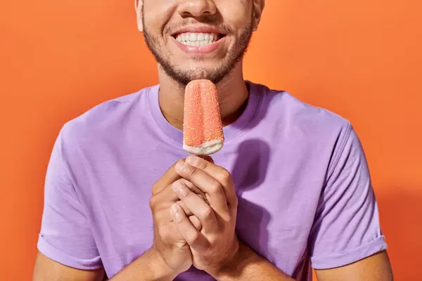 Foto recortada de hombre afroamericano sosteniendo helado con salpicaduras sobre fondo naranja - foto de stock