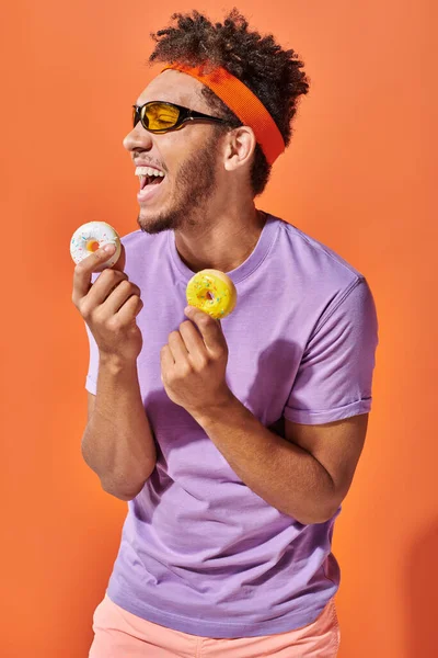 Молодий афроамериканський чоловік в сонцезахисних окулярах тримає папуги розміром з укус і сміється на помаранчевому фоні — стокове фото