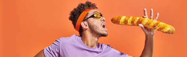 Bannière, homme afro-américain en lunettes de soleil et bandeau tenant baguette fraîche sur fond orange — Photo de stock