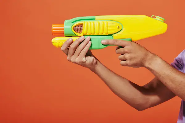 Cropped shot of african american man playing water fight with toy gun on orange background — Stock Photo