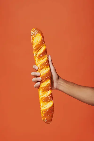 Cropped view of person holding freshly baked baguette on orange background, crunchy french bakery — Stock Photo