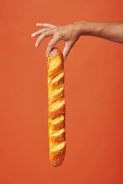 Tiro recortado de la persona que sostiene la baguette recién horneada sobre fondo naranja, panadería francesa crujiente - foto de stock