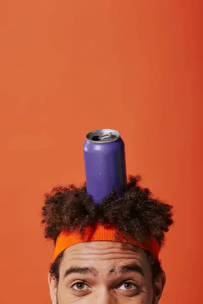 Purple soda can on head of curly african american man with headband on orange background — Stock Photo