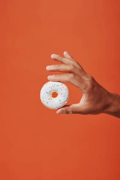Vista cortada de pessoa segurando donut de baunilha envidraçada com polvilhas sobre fundo laranja, cobertura branca — Fotografia de Stock