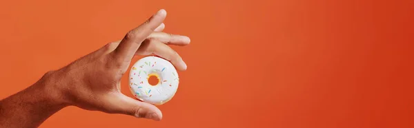 Banner recortado de pessoa segurando donut de baunilha envidraçado com polvilhas no fundo laranja — Fotografia de Stock