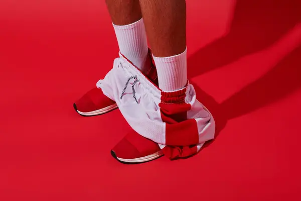 Foto conceptual, hombre recortado en zapatillas de deporte, calcetines blancos y corredores de pie sobre fondo rojo - foto de stock