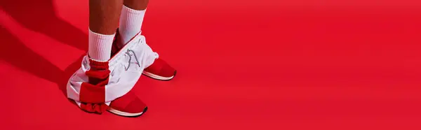 Estandarte conceptual, piernas masculinas en zapatillas de deporte, calcetines blancos y corredores sobre fondo rojo - foto de stock