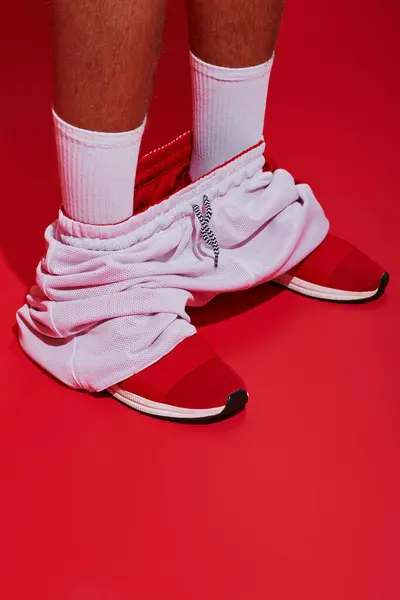 Fotografía de moda, chico recortado en zapatillas de deporte, calcetines blancos y corredores de pie sobre fondo rojo - foto de stock