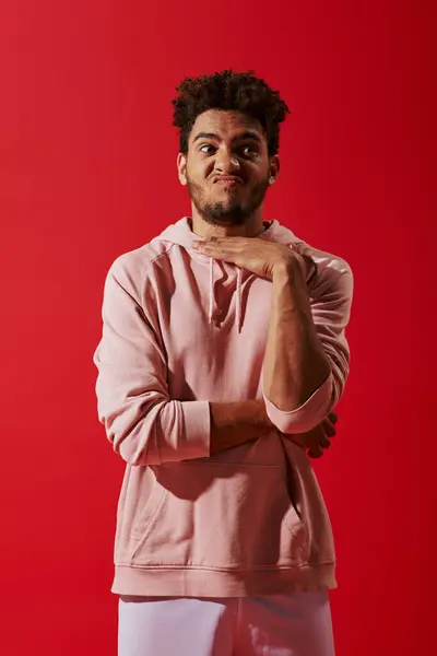 Confuso homem afro-americano em roupas de ginástica gesticulando e amuando lábios em fundo vermelho — Fotografia de Stock