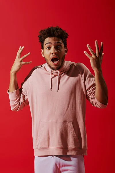 Confused african american man in gym clothes gesturing with opened mouth on red background — Stock Photo