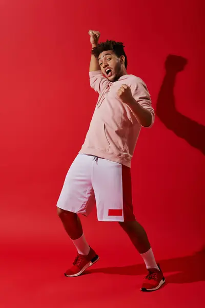 Збуджений афроамериканський чоловік у спортивному одязі радіє і дивиться на камеру на червоному тлі — стокове фото