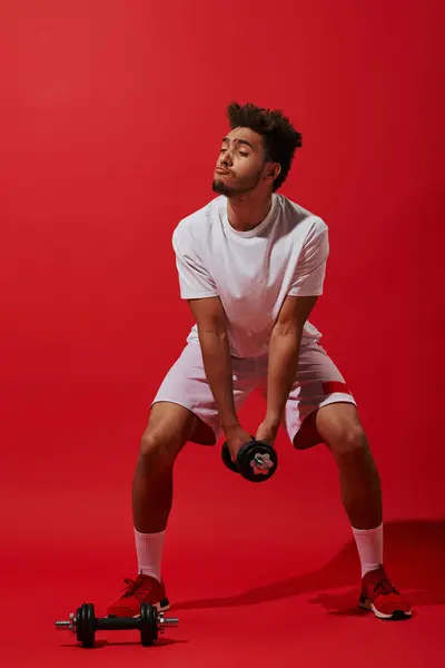 Full length of funny african american sportsman exercising with dumbbell on red background — Stock Photo