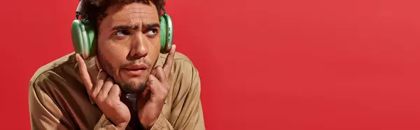 Banner of confused african american man in wireless headphones listening music on red background — Stock Photo