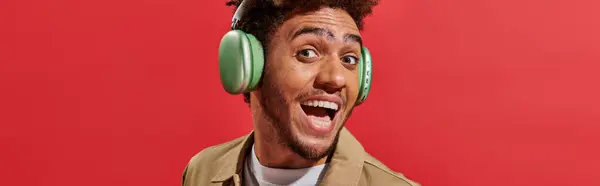 Banner eines aufgeregten afrikanisch-amerikanischen Mannes in drahtlosen Kopfhörern mit offenem Mund auf rotem Hintergrund — Stockfoto