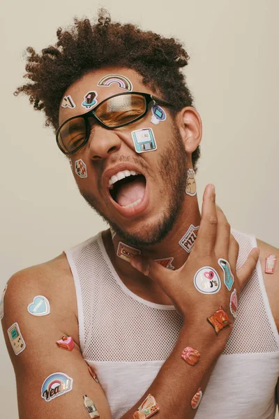 Expressive african american man in sunglasses with trendy stickers on face on grey background — Stock Photo