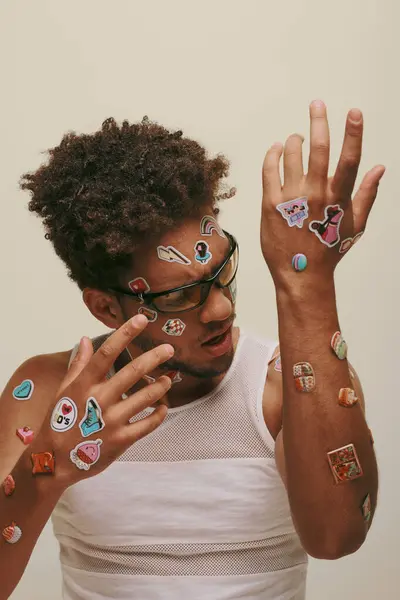 Amazed african american man in sunglasses looking at trendy stickers on his body on grey background — Stock Photo