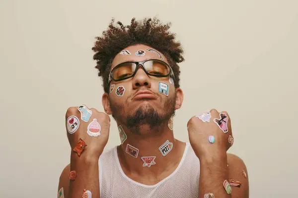 Afro-américain en lunettes de soleil avec des autocollants sur le visage en regardant la caméra sur fond gris — Photo de stock