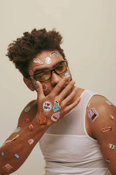 African american guy in sunglasses with stickers on face covering mouth on grey background — Stock Photo
