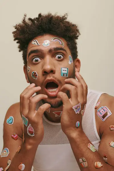 Shocked african american guy in tank top with stickers on face looking at camera on grey background — Stock Photo