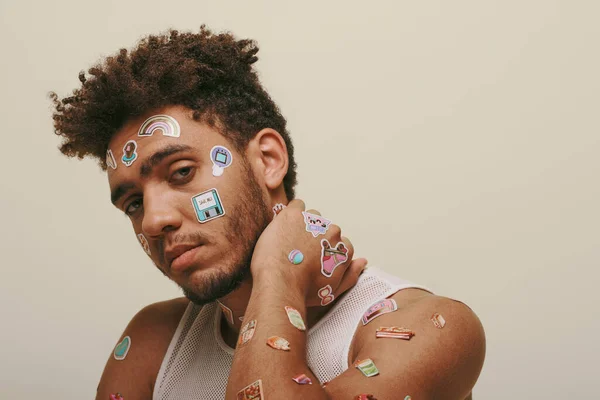 African american guy in tank top with stickers on face looking at camera on grey background — Stock Photo