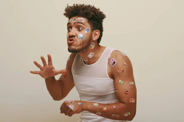 Expressive african american man with stickers on face grimacing and gesturing on grey background — Stock Photo