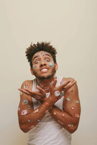 Емоційний афроамериканський чоловік з наклейками на обличчі жестикулює на сірому фоні, хіпстер — стокове фото