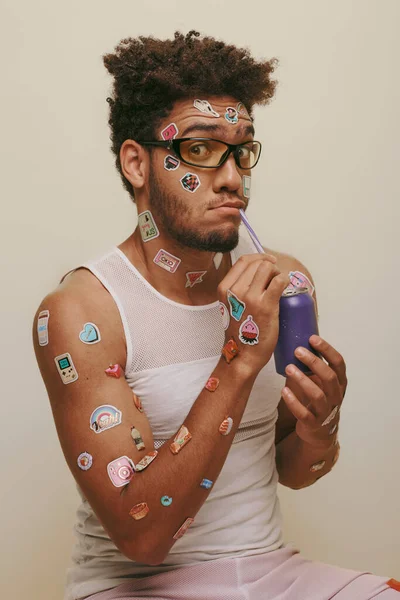 Jovem afro-americano com adesivos no rosto e corpo bebendo refrigerante no fundo cinza — Fotografia de Stock