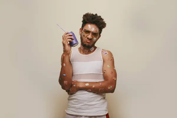 Triste afro-americano homem com adesivos no rosto e corpo segurando lata de refrigerante no fundo cinza — Fotografia de Stock