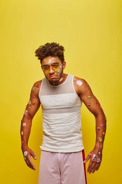 Unzufriedener junger afrikanisch-amerikanischer Mann mit Aufklebern im Gesicht und Körper auf gelbem Hintergrund — Stockfoto