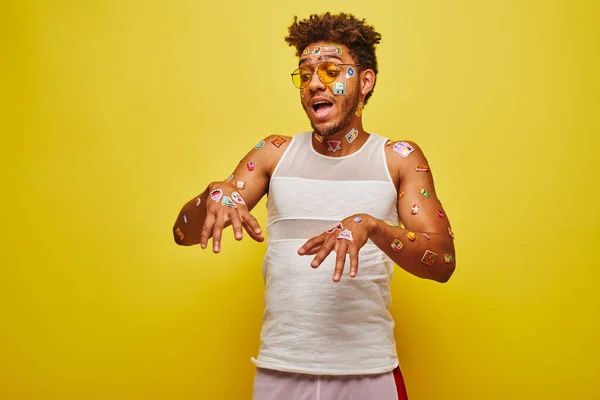 Playful african american man looking at stickers on his hands and body on yellow background — Stock Photo