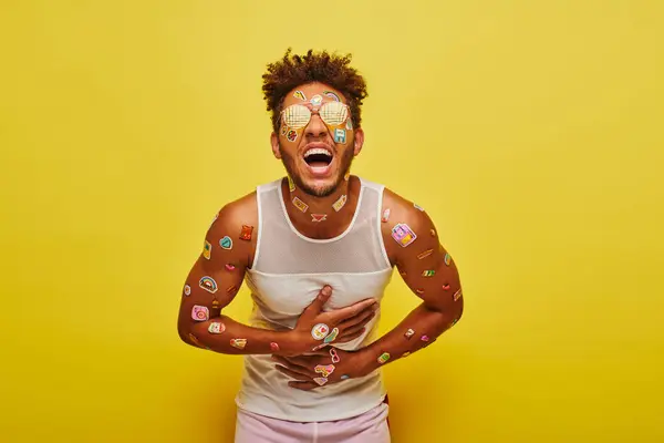Excited african american man with stickers on his face and body laughing on yellow background — Stock Photo
