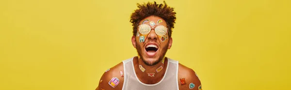 Jolly african american man with stickers on his face and body laughing on yellow background, banner — Stock Photo