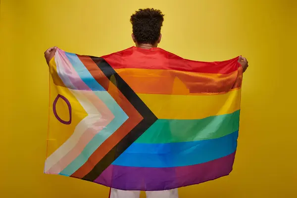 Back view of african american man holding lgbtq rainbow flag on yellow background, pride month — Stock Photo