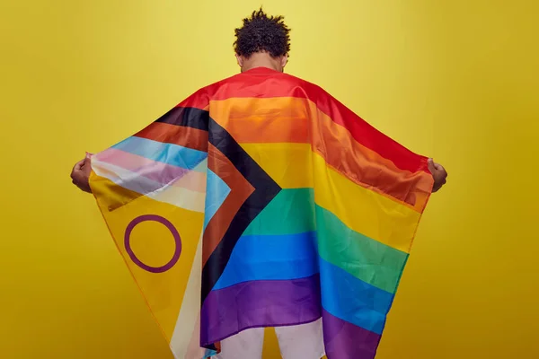 Back view of african american guy holding rainbow lgbt flag on yellow background, pride month — Stock Photo