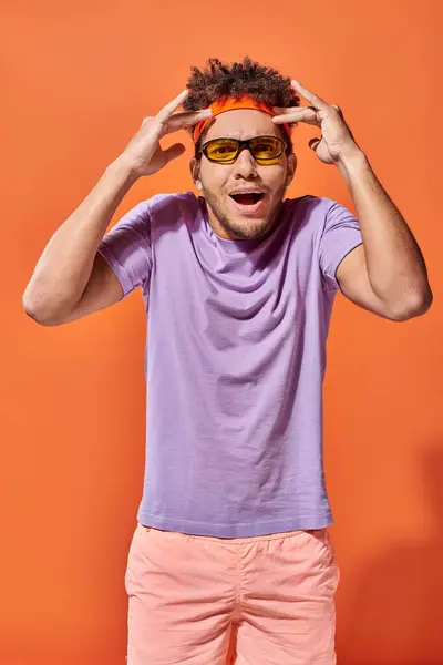 Stupito afro americano uomo in fascia e occhiali da sole gesticolando su sfondo arancione, strabiliante — Foto stock
