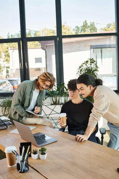 Young man with coffee to go discussing startup project with his male colleagues over laptop — Stock Photo