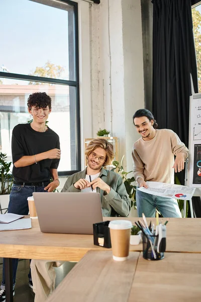 Cheerful entrepreneurs in their 20s brainstorming on project at a coworking space, looking at laptop — Stock Photo