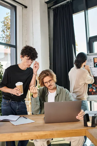 Jeunes hommes d'affaires évaluant les données sur ordinateur portable avec un collègue regardant les graphiques en arrière-plan, démarrage — Photo de stock