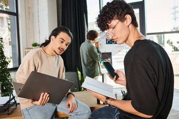 Jovens profissionais com laptop e smartphone discutindo projeto de inicialização, homens na casa dos 20 anos — Fotografia de Stock