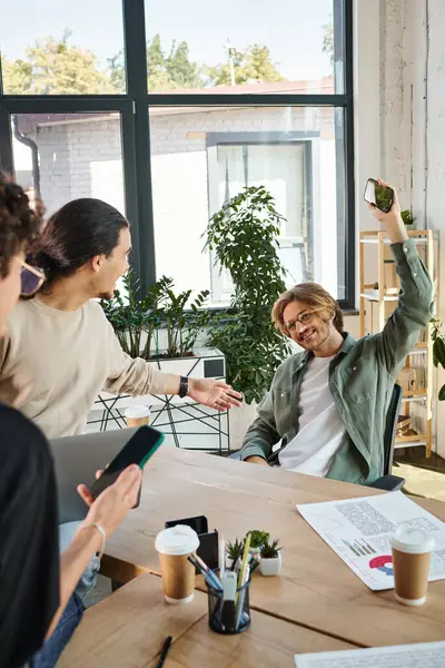Startup team in office brainstorming with gadgets, happy man in 20s raised hand with smartphone — Stock Photo
