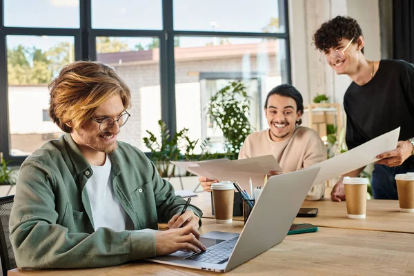 Счастливый человек с ноутбуком, команда молодых предпринимателей, занимающихся планированием проектов в офисе — стоковое фото