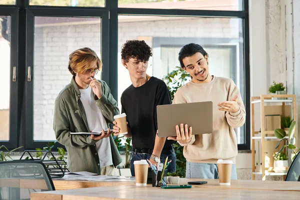 Three young men engaged in a lively discussion over a laptop at a coworking space, startup ideas — Stock Photo